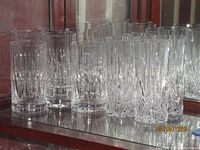 Photo showing group of crystal glassware in two patterns arranged on mirrored surface. Includes five glasses with vertical cuts on left and seven glasses with diamond/fan cuts on right.