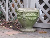 Large green stone pot with detailed Greek key and grape design on patio