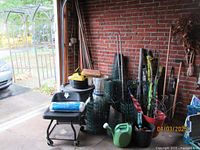 Photo showing large group of garden fencing rolls, various stakes, plastic sheeting, buckets, and gardening tools arranged in a garage space.