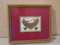 Framed golden art handcrafted beaded necklace with earrings mounted on red matting in a gold-colored frame.
