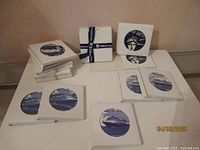 Fifteen white square coasters with blue circular Holland America Line cruise-themed images displayed in multiple stacks and a ribbon-bound bundle.