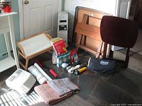 Wide view showing multiple home goods including Coleman bed in a bag, folding tray tables, space heater, rugs, flashlights and other small items.