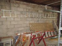 Aluminum extension ladder mounted on wall with stabilizer and partially visible wooden horses and red saw horses