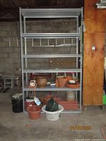 Front view of metal shelf unit with various pots and containers placed on the lower shelves and floor near it.