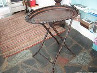 Full view of the metal folding tray table standing on stone floor with twisted metal legs and oval tray.