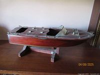 Wooden model boat resembling classic Chris Craft double cockpit runabout boat, viewed from side on display stand