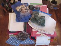 Overview of assorted cloth napkins folded including blue napkins, white napkins, some shells and wooden rings packaged in plastic, and pink and patterned napkins underneath.