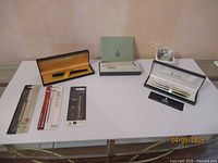 Overview of all pens and refills including the Waterman fountain pen box, Bill Blass and Cross boxed pen sets, and refill packages on a table.