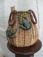 Side view showing two green frog figurines climbing the vase with vine-shaped handles and drip glaze.