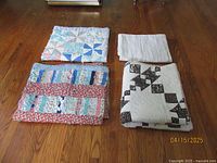 Four folded quilts displayed on a wood floor showing various colors and patterns