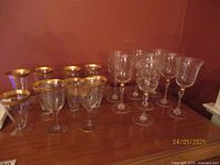Photo of all stem glasses arranged on a wooden surface showing various styles with gold accents, includes both sets of glasses and the two individual glasses.