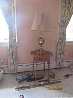 Full view of round tiger maple side table topped with brass lamp, room backdrop
