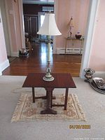Front view of vintage mahogany drop-leaf table with candlestick lamp and small rug underneath