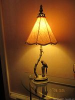 Full view of the lamp lit on a glass table showing the unique faux bamboo textured base with parrot figurine and flared textured glass shade.