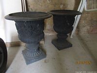 Pair of black cast iron urn planters side by side on concrete floor
