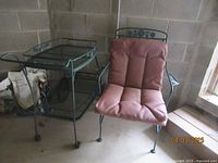 Side angle showing the wrought iron green bar tea cart with floral design and matching chair with pink cushion.