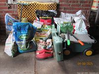 Overview showing bags of garden care products, Le Chameau red garden clogs, and garden rolling tool cart in an outdoor storage area.