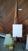 Large standing wood easel 65 inches tall supporting a blank canvas, wooden construction with adjustable support.
