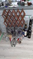 Photo showing expandable wooden wine rack behind two decorative metal wine racks, multiple clear glass decanters, vintage alcohol bottles, and a corker tool in front.