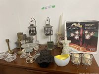 Photo of various candle holders and candles including brass, glass, ceramic, and metal types arranged on table