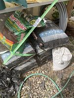 Five full bags of Hydrocorn substrate stacked under a shelf alongside a 3/4 full green bag of Scotts Turf Builder grass seed, all bags secured with green straps.