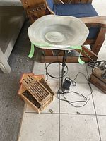 Full view of birdbath style fountain with glass bowl on metal stand beside wooden mason bee hive.