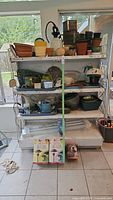 Full view of multiple shelves containing assorted garden pots, watering cans, spray bottles, and garden items.