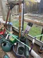 Full overview of the lot including rakes, watering cans, clothespole, rolls of weed control fabric, garden hose, and irrigation equipment.