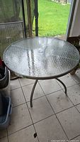 Full view of round outdoor table with textured glass top and three metal legs.