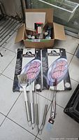 Full lot view showing two Grill Pro boxed serving platters, stainless steel BBQ tools, and a cardboard box with miscellaneous items.