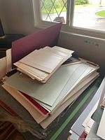 Stack of assorted mat boards and backing materials of various colors and sizes placed on table near window.