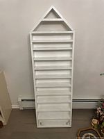 Front view of the white wooden standing shelf tall with multiple shelves and triangular top.