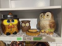 Wide shot showing two owl cookie jars, one planter, and extra lid on a shelf.