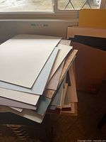 Photo showing a large stack of assorted picture matting boards in various colors including cream, blue, brown, black, and patterned varietals, placed near a window.
