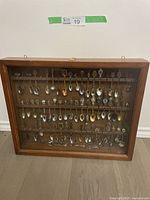 Full front view of wooden display case with glass showing rows of commemorative spoons.