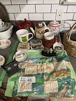 Overview of assorted teapots, mugs, napkin holder, napkin rings, spoon rest, coasters, and animal teatowel
