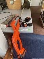 Black & Decker cordless weed trimmer and two extra 20V batteries on a grey surface.