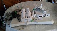 Overview of Wii system components on round table including console, balance board, charging dock with two remotes, power adapter, and cables.