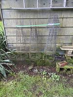 Six wire plant supports of various sizes arranged vertically against an outdoor wall in grassy area.