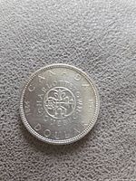Reverse side of 1964 Canadian silver dollar commemorative coin with floral emblem representing Canada’s founding cultures and date marks