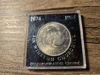 Top view of the commemorative crown coin showing Sir Winston Churchill's portrait in the protective case with inscription and dates visible.
