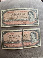 Front side of two 1954 Canadian $2 banknotes, showing bilingual text and Queen Elizabeth II portrait, one banknote torn in half.