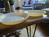 Two vintage Fire King peach lustre pie plates on a wooden table with a natural light background.