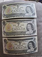 Front side of three 1973 Canadian one-dollar bills, showing Queen Elizabeth II and serial numbers.