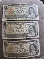 Front sides of three 1973 Canadian one-dollar bills showing portrait of Queen Elizabeth II, serial numbers visible including sequential numbers on bottom two bills.