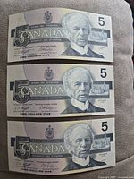Front sides of three 1986 Canadian $5 banknotes showing Sir Wilfred Laurier portrait and design details.