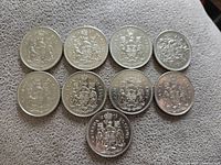Nine Canadian 50 cent coins arranged in two rows, showing the reverse side with the Canadian Coat of Arms.