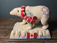 Front view of the polar bear figurine showing red and white scarf, purple patches, and Canadian flag on base.
