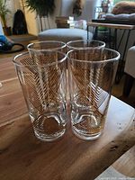 Four tall clear glass highball tumblers with gold geometric patterns arranged closely on wooden table.