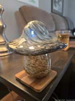 Side angle photo of hand blown toadstool glass showing detailed swirls in the cap and speckled stem on a wooden base.